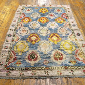 Colorful shaggy rug with large yellow, red, and cream medallions on blue, laid over glossy wood floors.