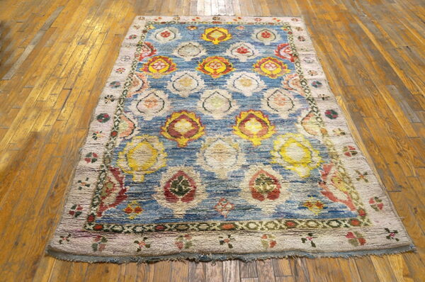 Colorful shaggy rug with large yellow, red, and cream medallions on blue, laid over glossy wood floors.