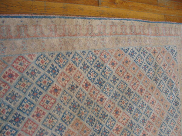 Beige rug with a diamond lattice field pattern in faded blue and pink on natural wood floor.