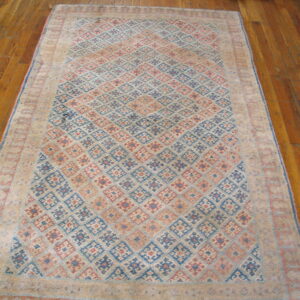 Beige, blue, and red geometric rug with diamond motifs lying on a polished wood plank floor.