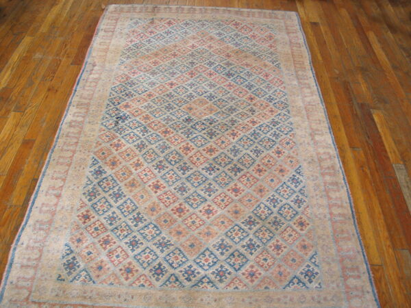 Beige, blue, and red geometric rug with diamond motifs lying on a polished wood plank floor.