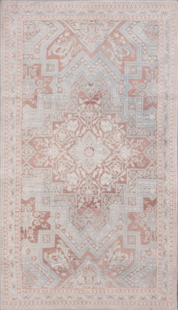 Distressed traditional rug with a central medallion pattern in faded rose, pale blue, and ivory tones.