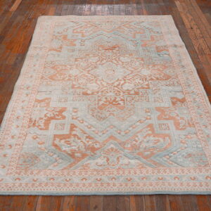 Traditional peach and light blue rug with a textured pile rests on polished dark wood floorboards.