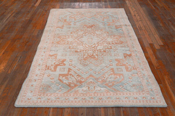 Traditional peach and light blue rug with a textured pile rests on polished dark wood floorboards.