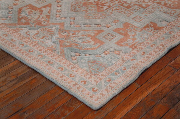 Corner of a textured blue and peach geometric rug lying on reddish-brown hardwood planks.