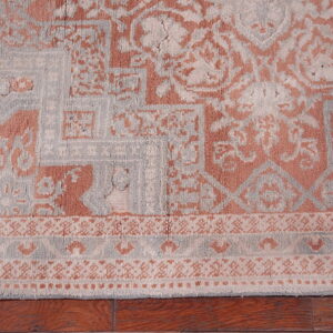 Textured low-pile rug with salmon and light gray geometric medallion patterns resting on wood floors.