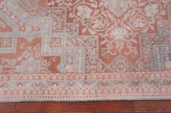 Textured low-pile rug with salmon and light gray geometric medallion patterns resting on wood floors.