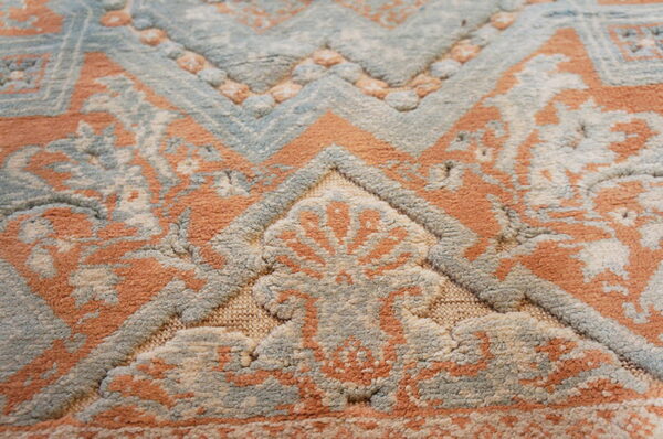 Detail of a high-low pile rug showing distressed blue, orange, and beige colors in a geometric floral design.