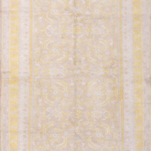 Rectangular, low-pile rug displaying faded traditional motifs and borders in yellow and light beige.