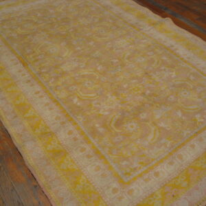 Distressed traditional rug in gold and light pink with a medallion pattern on dark wood flooring.