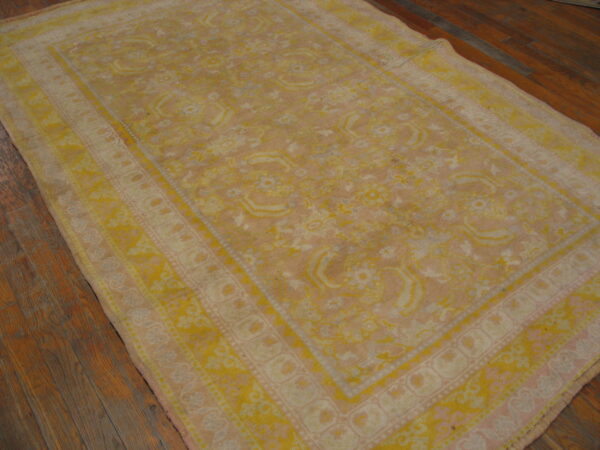 Distressed traditional rug in gold and light pink with a medallion pattern on dark wood flooring.