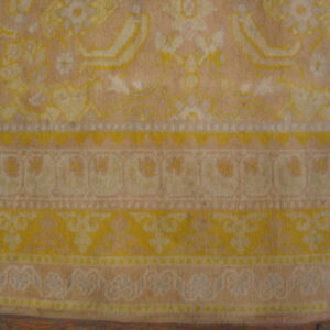 Detail of a faded traditional rug border with yellow, cream, and peach floral patterns over wood flooring.