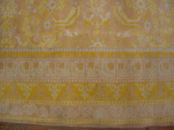 Detail of a faded traditional rug border with yellow, cream, and peach floral patterns over wood flooring.