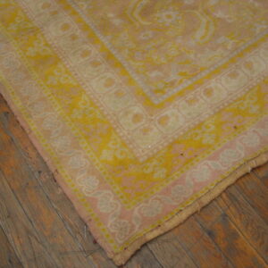 Corner view of a blush pink and yellow traditional rug with borders on plank wood flooring.