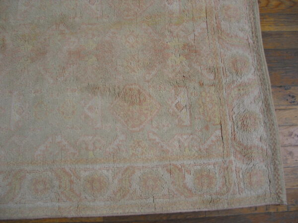 Close-up of a low-pile rug with faded pink, yellow, and beige traditional patterns on brown hardwood flooring.