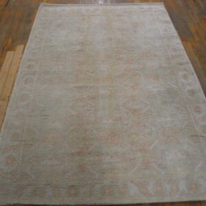 Pale sage and peach distressed rug with traditional motifs sits on dark plank hardwood flooring.