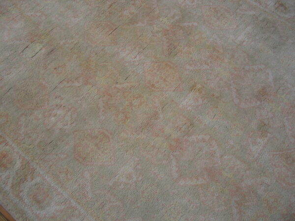Distressed rug surface in muted gray and faded pink colors showing a low-contrast traditional pattern.