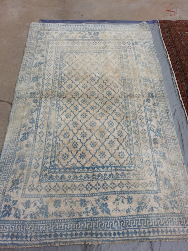 Distressed blue and cream high-pile rug with geometric and floral patterns, displayed on a concrete floor.