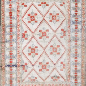 A high-pile rug featuring red, blue, and gray geometric diamond patterns on a distressed white field with patterned borders.