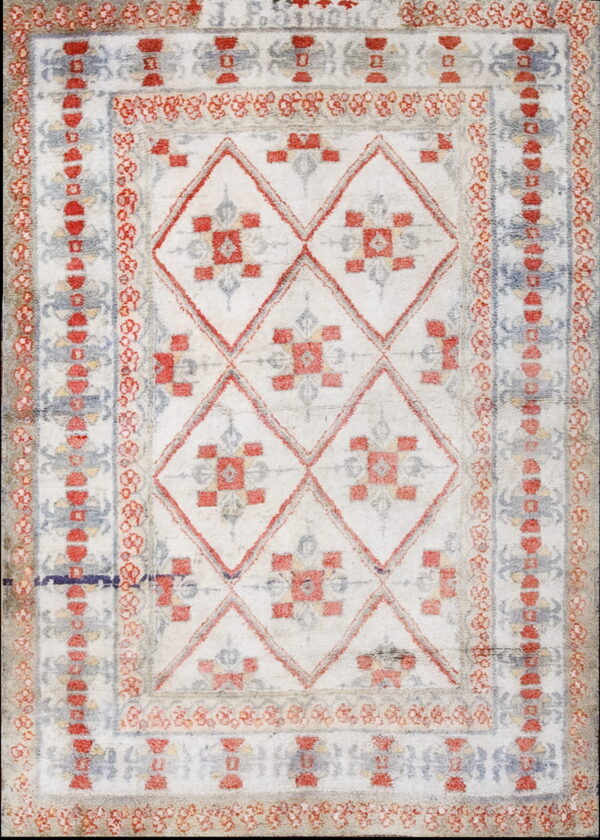 A high-pile rug featuring red, blue, and gray geometric diamond patterns on a distressed white field with patterned borders.