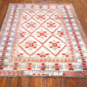 High-pile rug in ivory, red, and blue geometric diamond patterns sits on distressed wood flooring.
