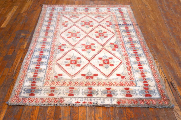 High-pile rug in ivory, red, and blue geometric diamond patterns sits on distressed wood flooring.
