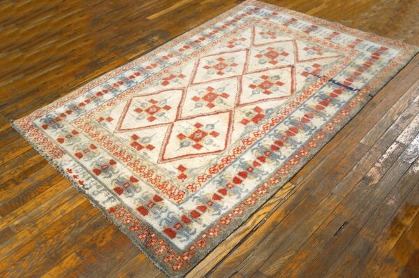 Cream, faded red, and blue geometric rug with a diamond pattern resting on wide, rustic wood plank flooring.
