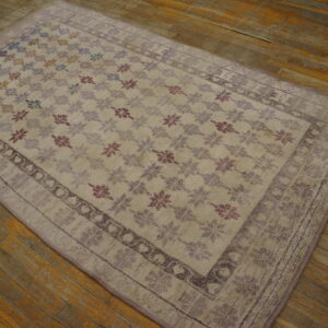 Light-colored rug with multicolored floral motifs and a purple border rests on worn wood flooring.