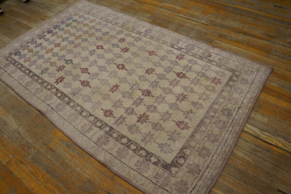 Light-colored rug with multicolored floral motifs and a purple border rests on worn wood flooring.