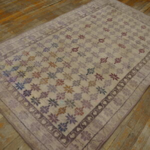 A low-pile lavender rug featuring a multi-colored floral pattern rests on a distressed wooden floor.