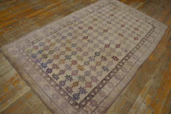 A low-pile lavender rug featuring a multi-colored floral pattern rests on a distressed wooden floor.