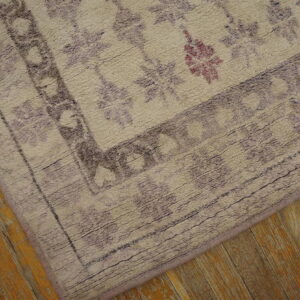 Textured, light-colored rug with purple geometric patterns and a border on distressed honey wood flooring.