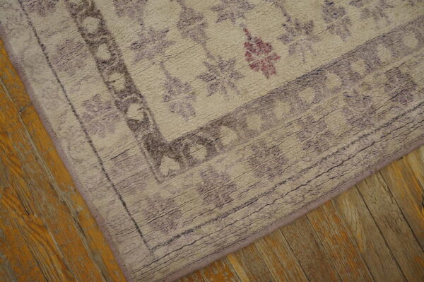 Textured, light-colored rug with purple geometric patterns and a border on distressed honey wood flooring.