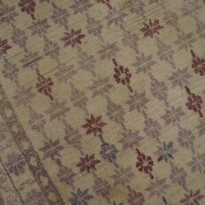 Distressed beige rug featuring faded maroon and purple floral motifs and a border on wood flooring.