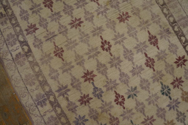 Distressed beige rug featuring faded maroon and purple floral motifs and a border on wood flooring.