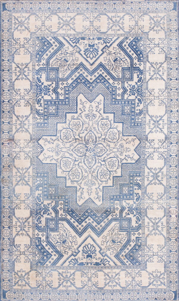Cream and faded blue rug with geometric tribal patterns surrounding a large floral medallion.