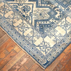 Cream and deep blue patterned rug with geometric and floral motifs on distressed wood planks.