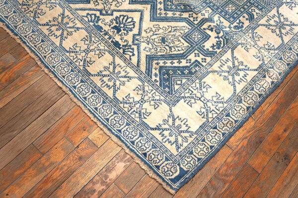 Cream and deep blue patterned rug with geometric and floral motifs on distressed wood planks.