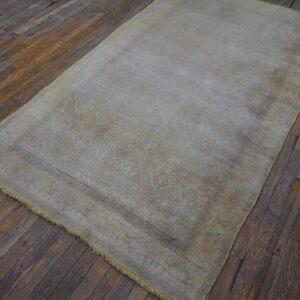 Low-pile beige and tan patterned rug with light fringe on dark, rustic wooden floorboards.