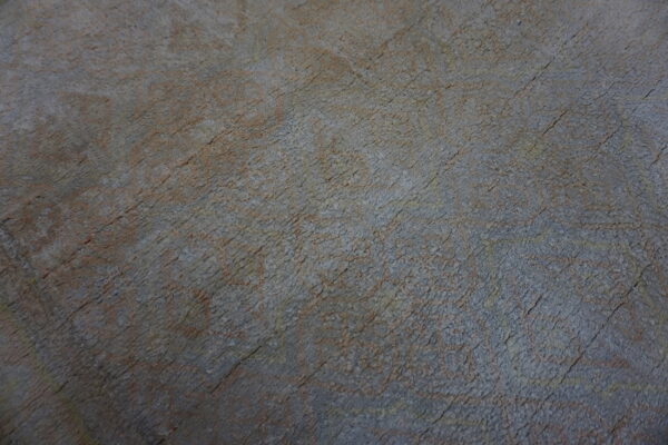Low-pile rug texture in faded blue-gray and rust colors with subtle, distressed patterns.