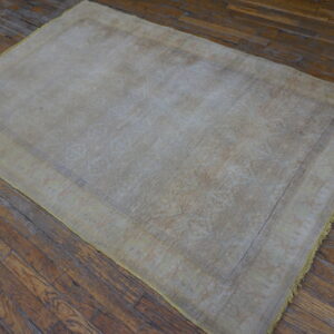 Lightly patterned beige and gray rug resting on dark, worn wooden floorboards.