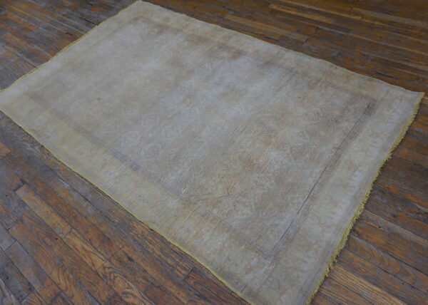 Lightly patterned beige and gray rug resting on dark, worn wooden floorboards.