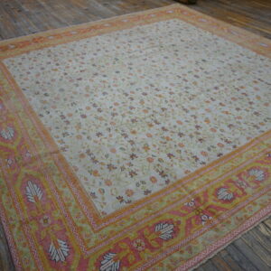 Low-pile rug with a cream floral field and pink, yellow, and orange ornate borders on a wood floor.