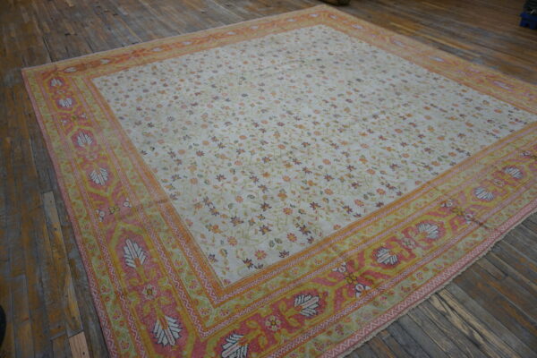 Low-pile rug with a cream floral field and pink, yellow, and orange ornate borders on a wood floor.