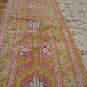 Medium-pile rug displaying pink, chartreuse, and cream colors with geometric borders and a scattered floral field.