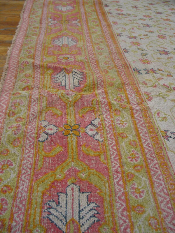 Medium-pile rug displaying pink, chartreuse, and cream colors with geometric borders and a scattered floral field.