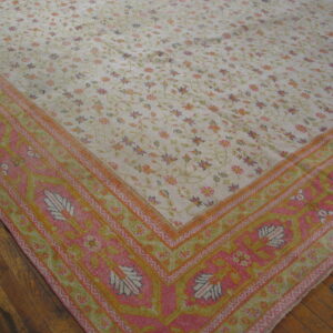 Pale cream floral rug featuring a wide, vibrant pink, orange, and green border on dark wood floors.