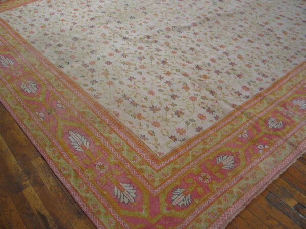 Pale cream floral rug featuring a wide, vibrant pink, orange, and green border on dark wood floors.