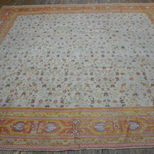 Cream floral rug with a wide pink and yellow border lies on rustic dark wooden floors.
