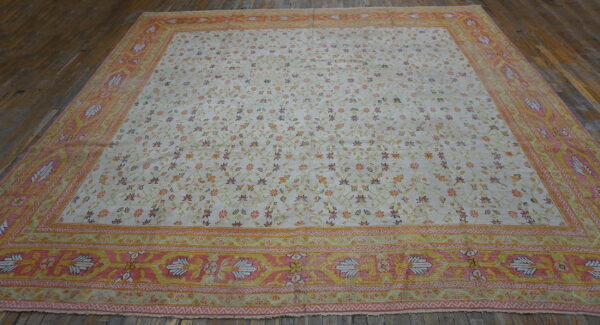 Cream floral rug with a wide pink and yellow border lies on rustic dark wooden floors.